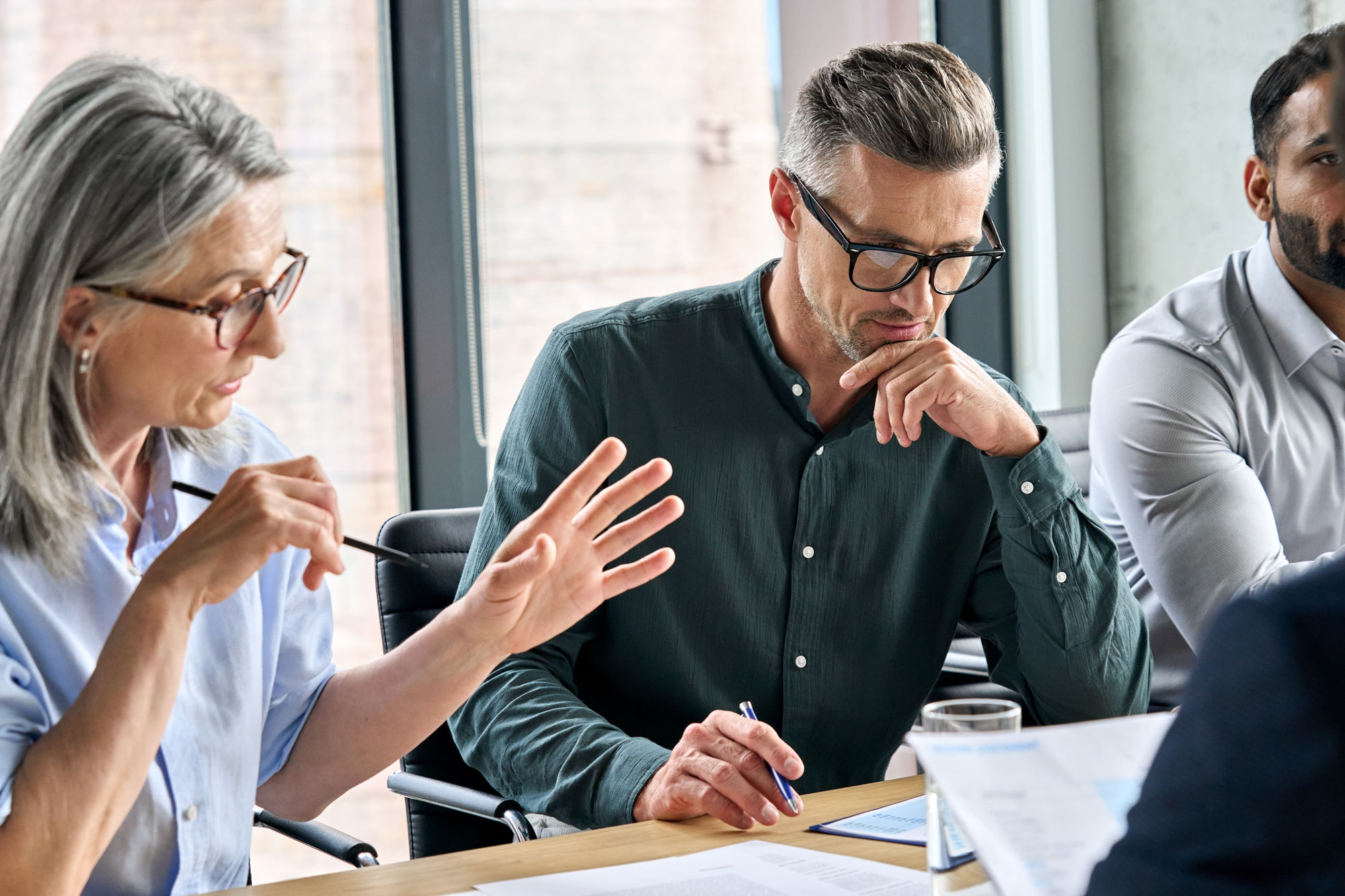 Serious ceo executive manager with business partner discussing corporation merge plan at board room table. Professional coworkers leaders doing paperwork in modern office.